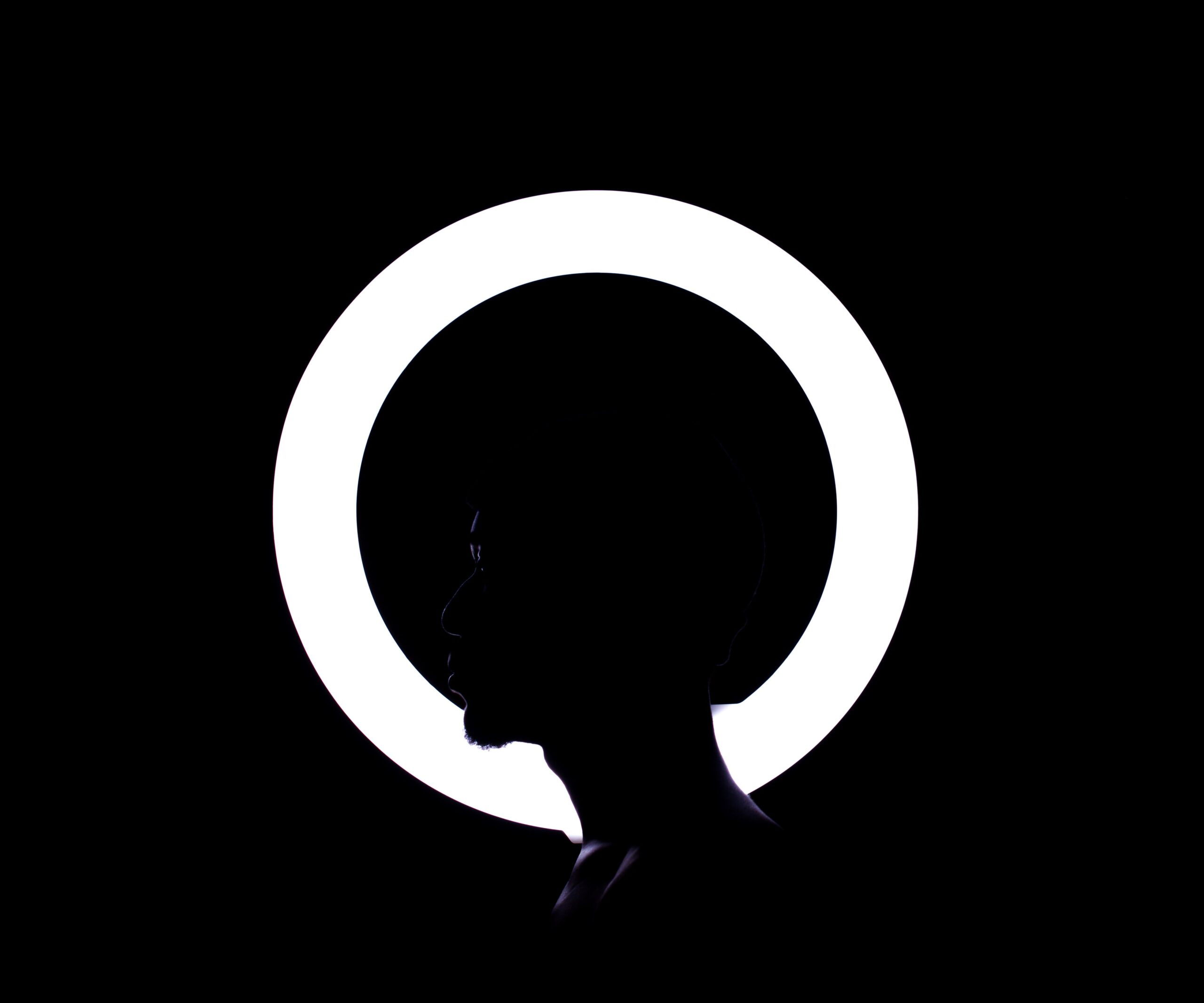Profile silhouette of a man with glowing ring light creating a dramatic halo effect in darkness.